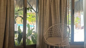 Una habitación con una silla colgante de macramé, un ventanal de vidrio que da a una piscina y cortinas.