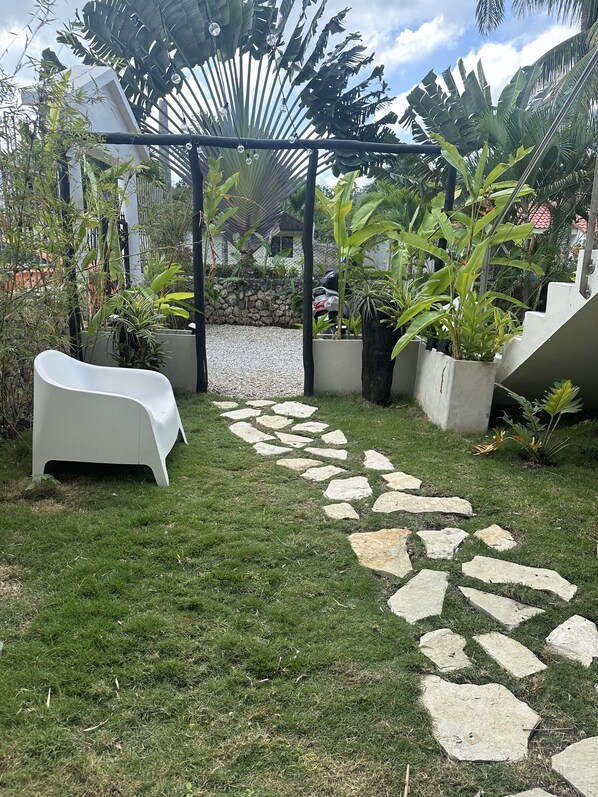A garden with a stone pathway, white outdoor furniture, and various plants.