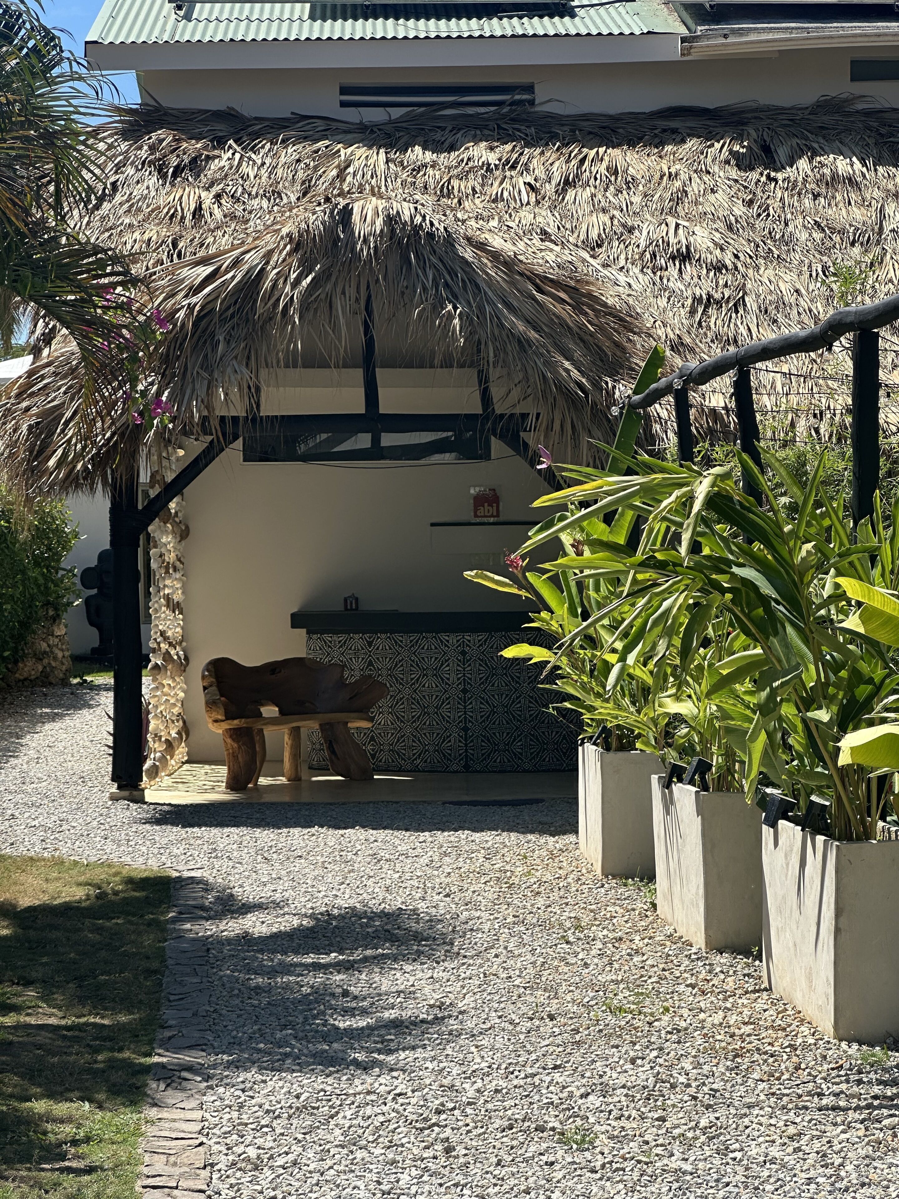 A covered outdoor seating area with a thatched roof, a wooden bench, and potted plants.