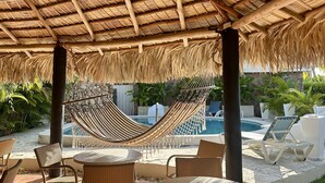 Un espacio de estar al aire libre cubierto con muebles de mimbre y una hamaca, con vista a una piscina.