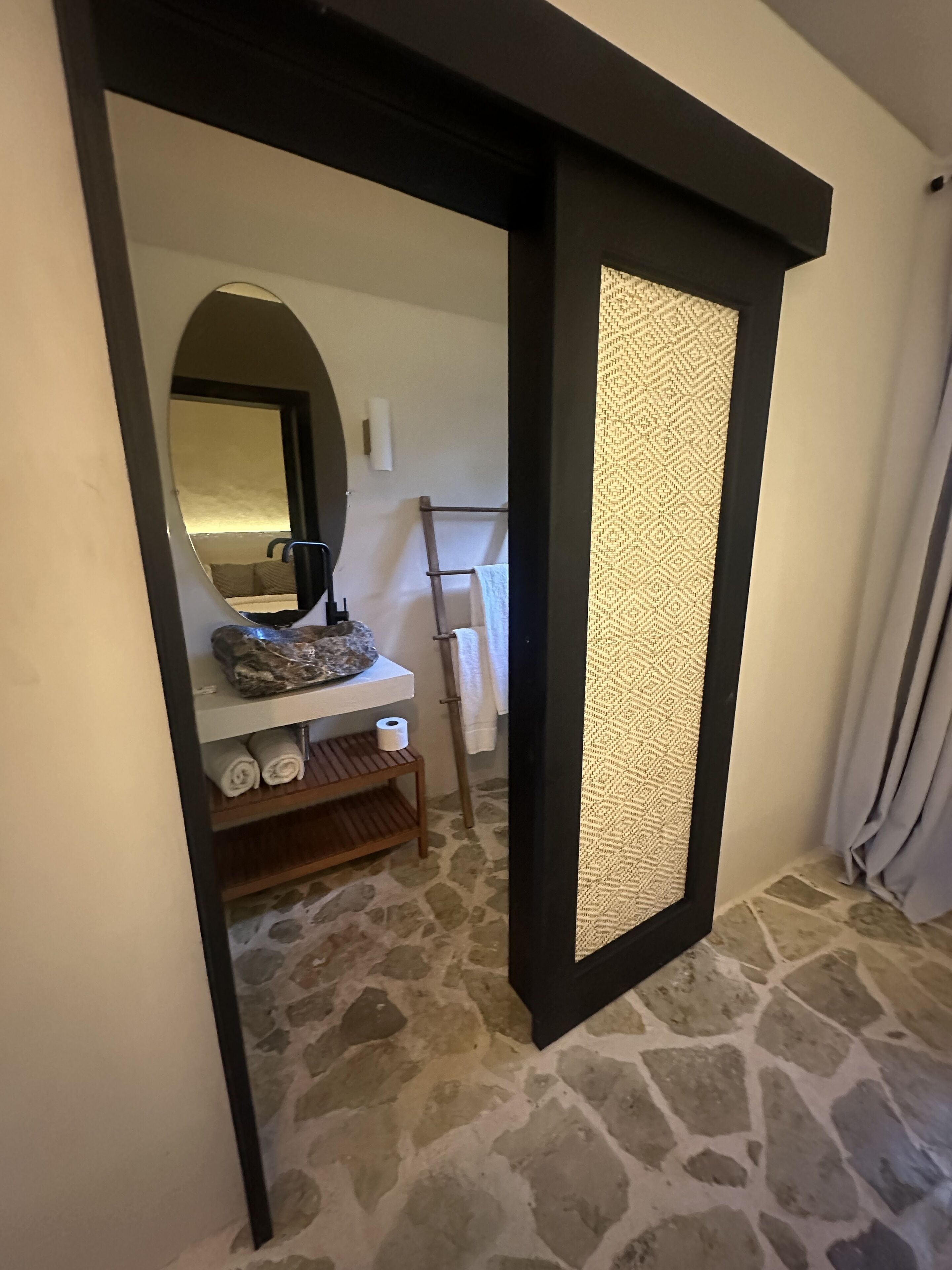 A bathroom with a stone floor, a sink with a mirror, and a towel rack.