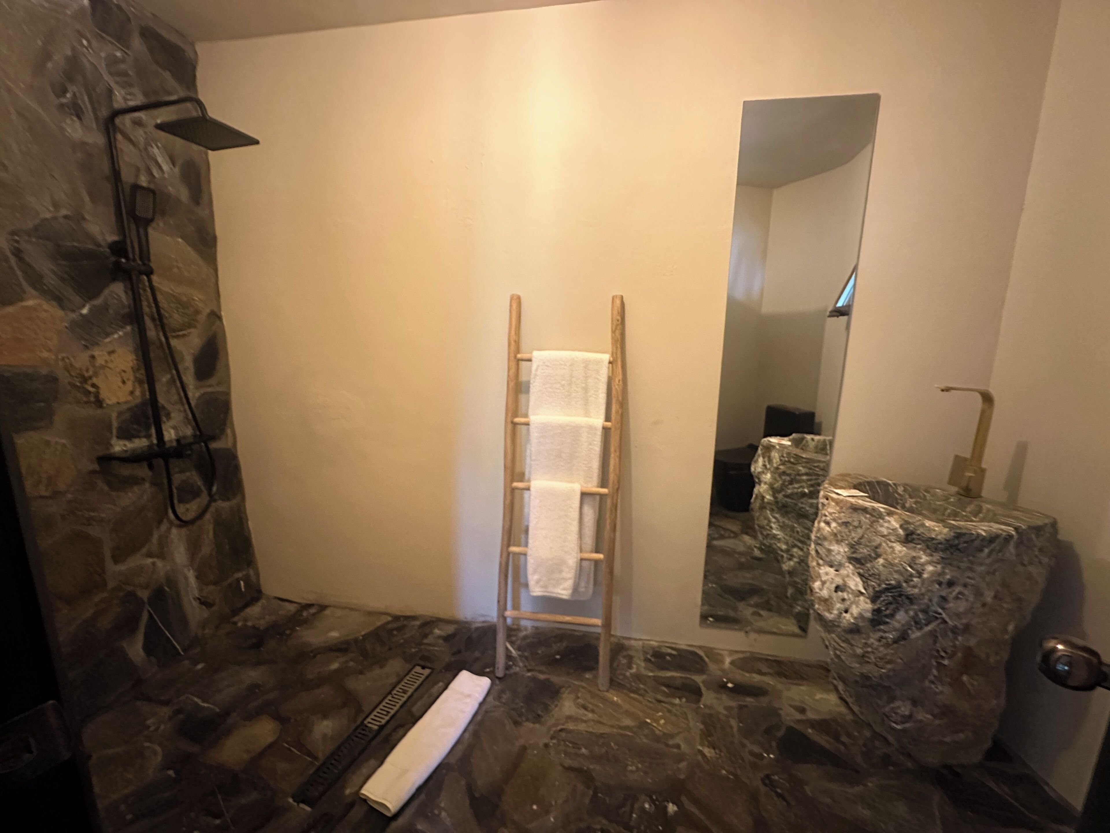 Een badkamer met een stenen muur, een houten ladder, een handdoek en een spiegel.