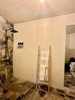 Un baño con pared de piedra, ducha, perchero de madera y espejo.
