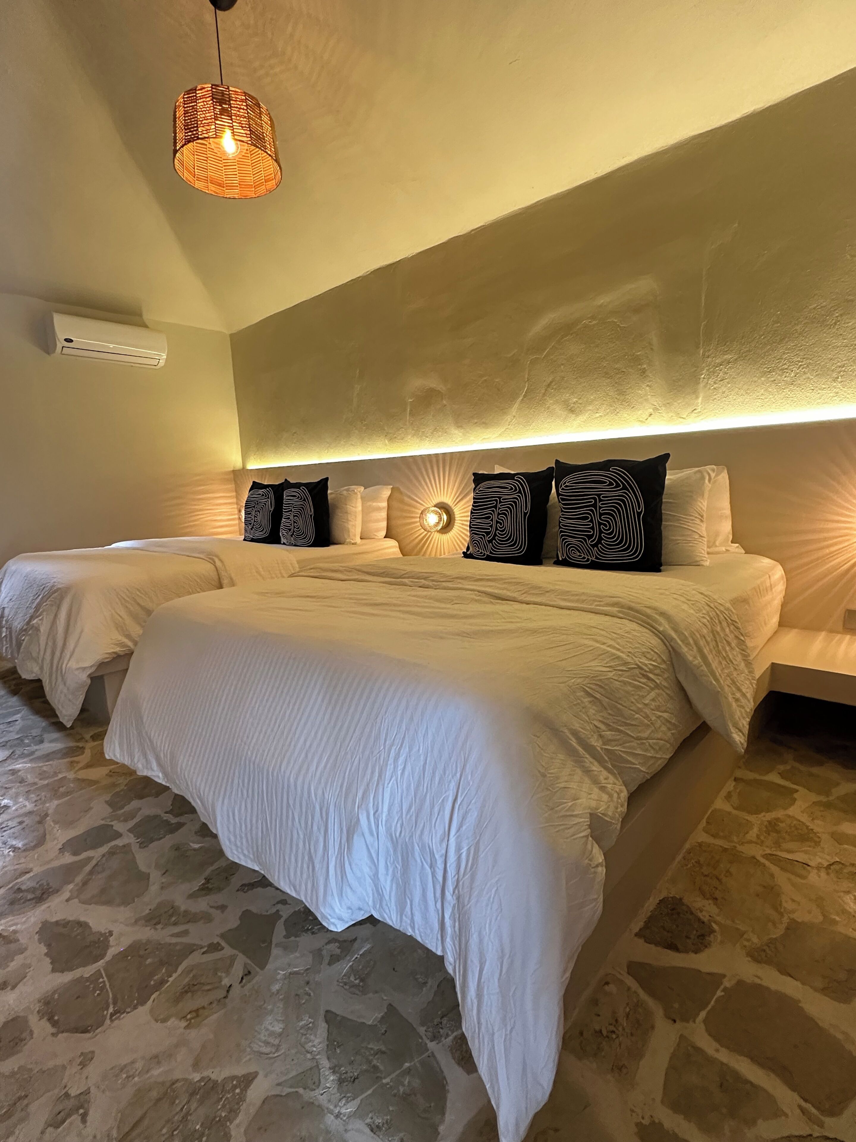 Un dormitorio con dos camas, suelo de piedra, ventilador de techo y aire acondicionado de pared.