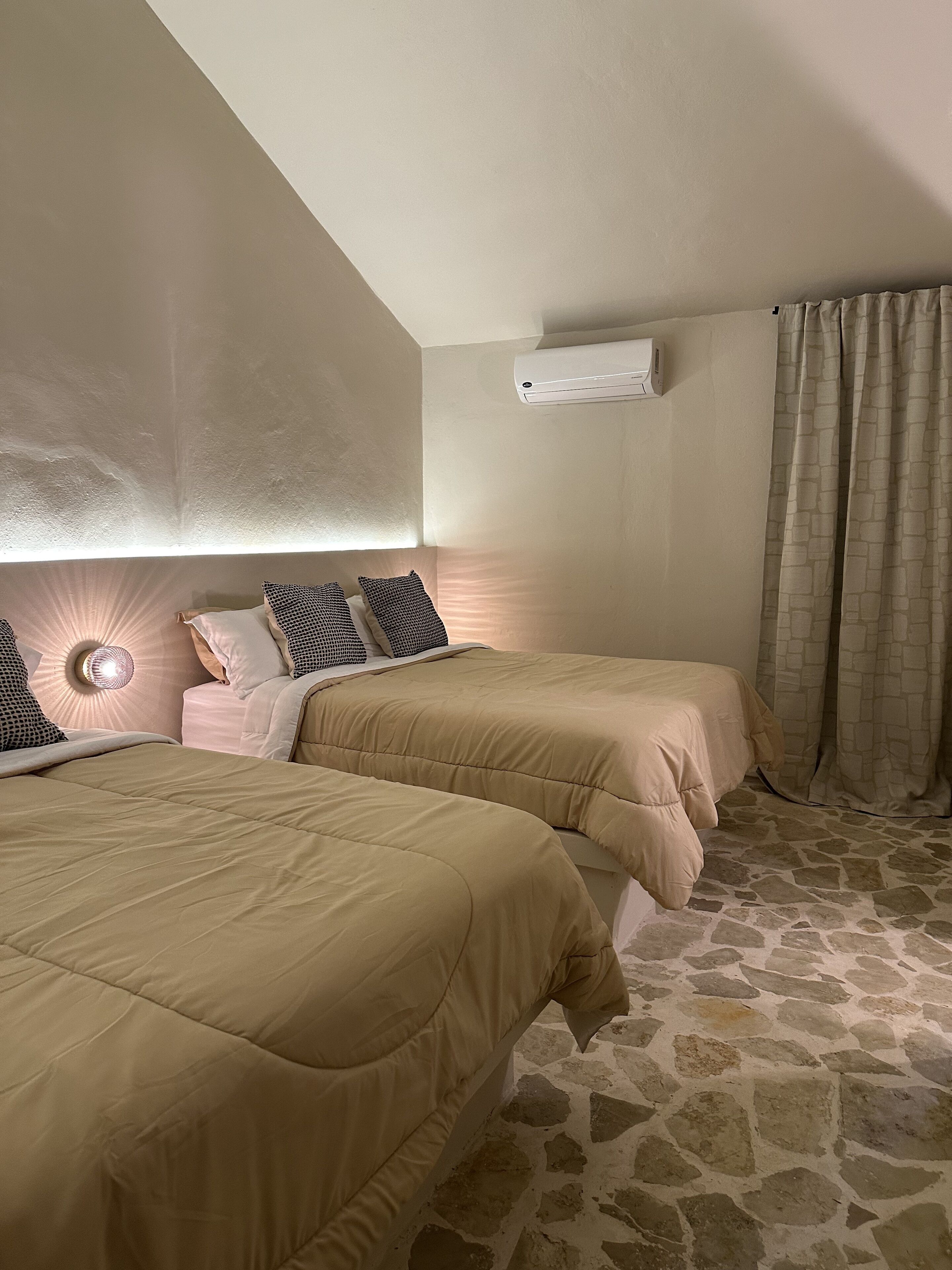 A bedroom with two beds, a stone floor, a ceiling fan, and a wall-mounted air conditioner.