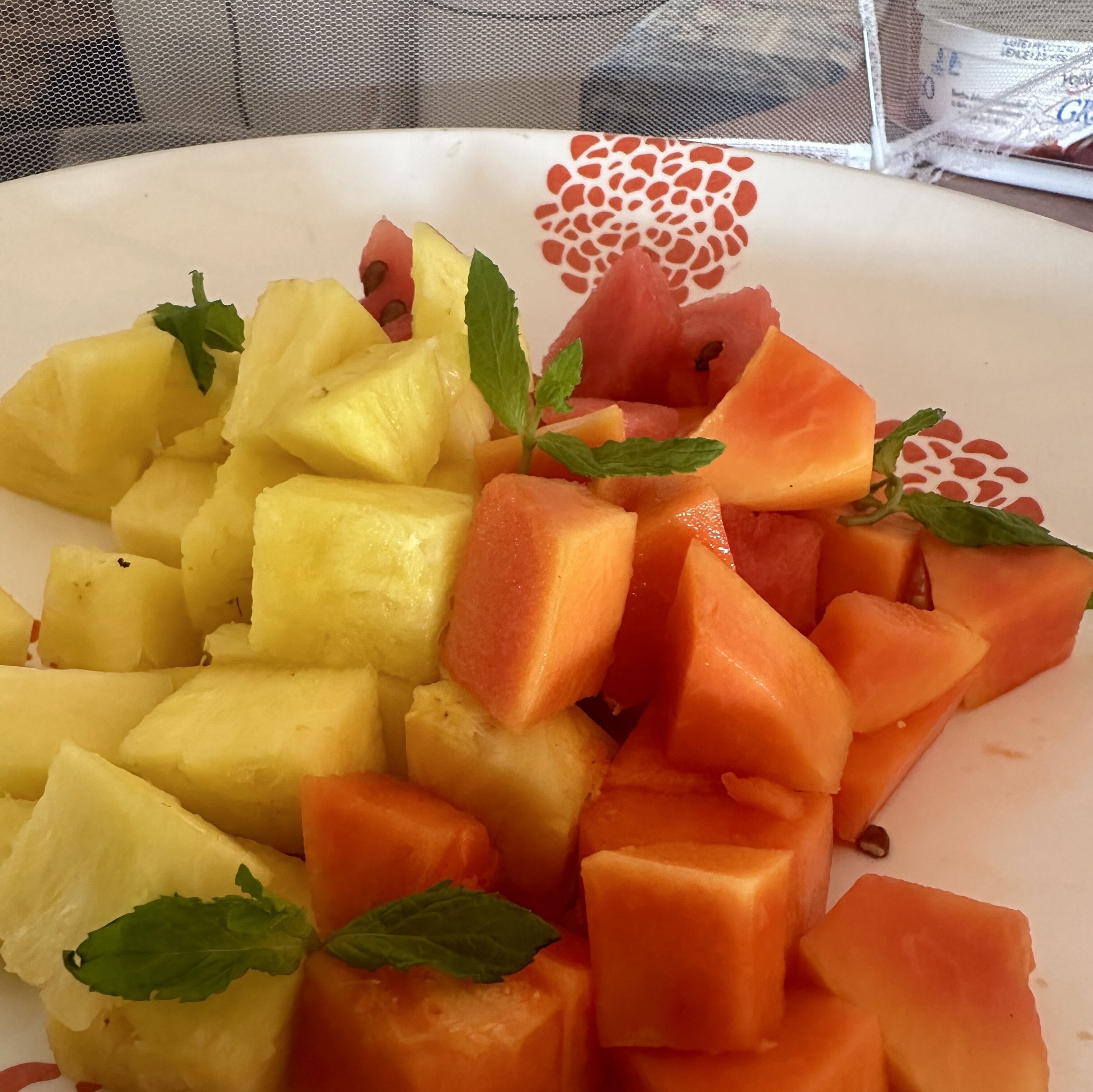 A plate of diced pineapple and cantaloupe with mint leaves.