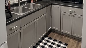 Una cocina con armarios blancos, encimera negra, pileta de acero inoxidable y microondas.