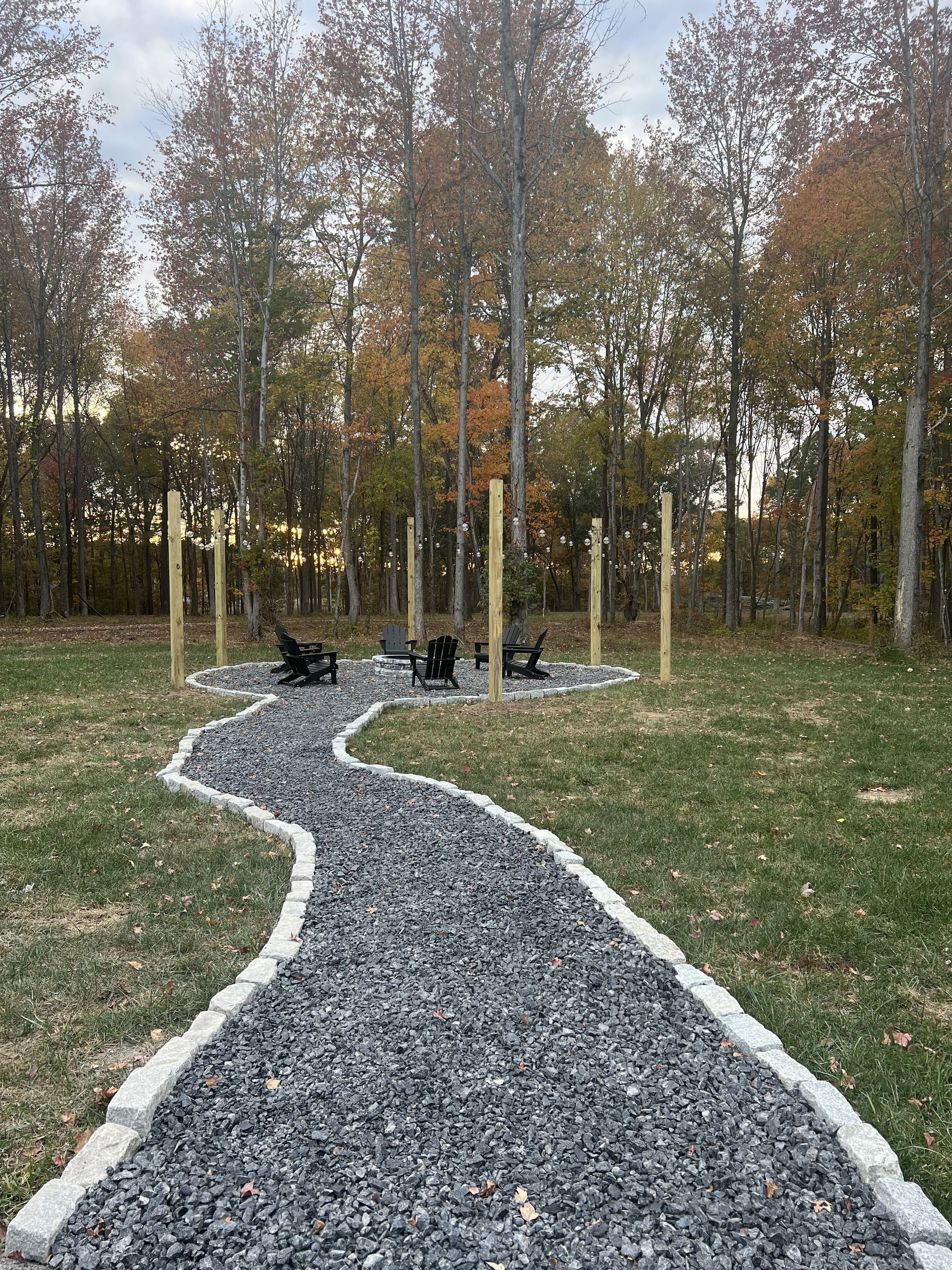 A gravel path leading to a seating area with benches and chairs, surrounded by trees with autumn foliage.
