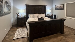 Un dormitorio con una cama grande, cabecera de madera oscura, dos mesitas de noche con lámparas, una alfombra y obras de arte en las paredes.