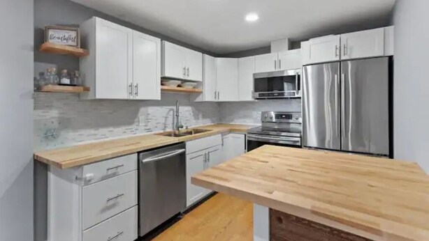 A modern kitchen with white cabinets, a stainless steel refrigerator, and a wooden countertop. - Exquisite Comfort: Luxury Suite (Portland)