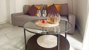 A modern living room with a glass coffee table, a grey sofa with patterned cushions, a decorative mirror, and a floor lamp. - AT - La higuera, Deluxe by VGH (Jerez de la Frontera)