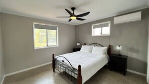 Un dormitorio con una cama individual, un ventilador de techo, dos mesitas de noche con lámparas y una ventana con persianas.