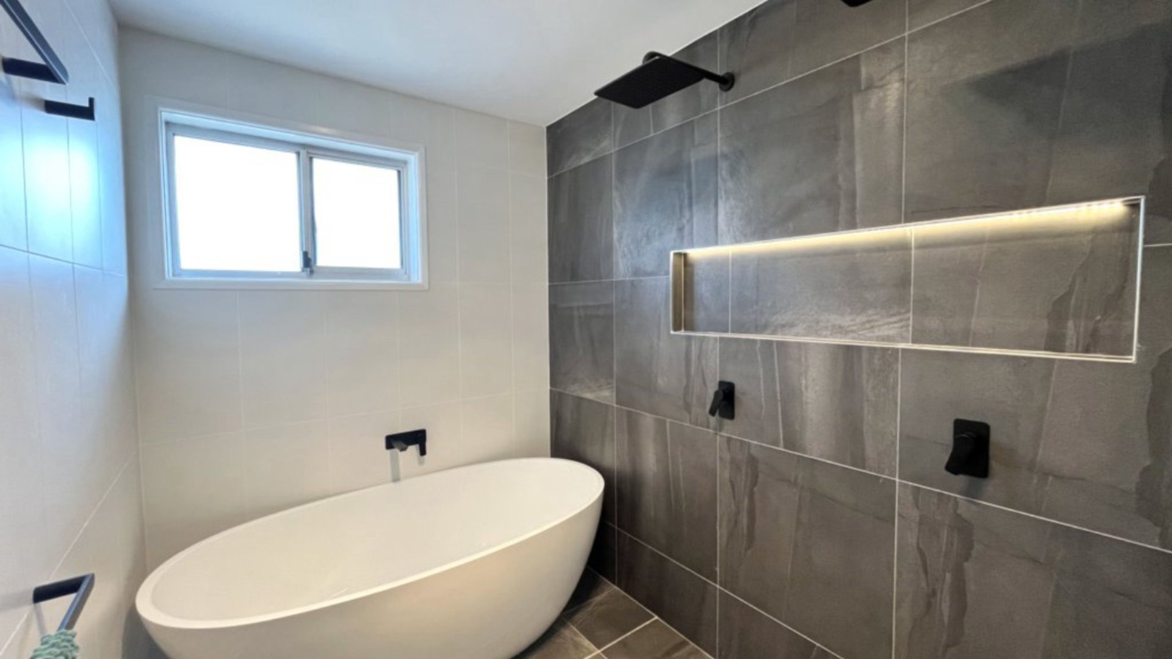 A modern bathroom with a freestanding bathtub, a window, and a wall-mounted light fixture.