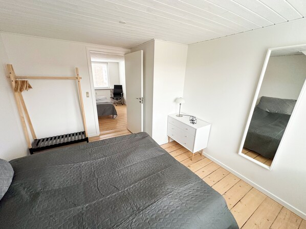 Et soveværelse med seng, kommode, spejl og udsigt til et andet rum.