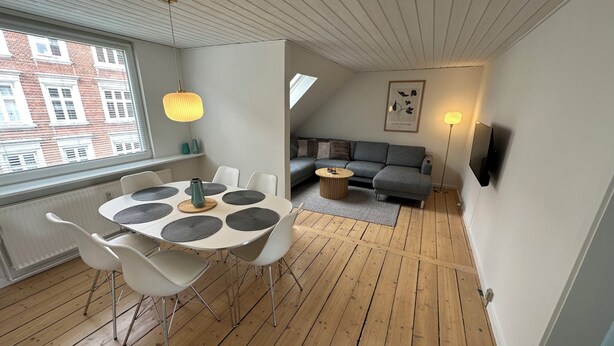 A modern living space with a dining table, white chairs, a grey sofa, and a wooden floor. - Modern apartment for 6 in city center (Aalborg)