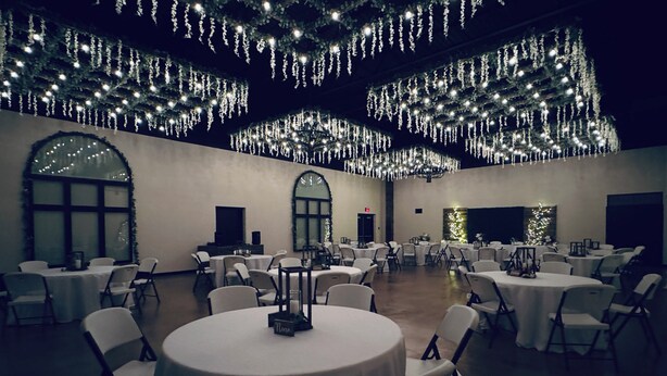 Une vaste salle de banquet dotée de tables et de chaises rondes, décorée de luminaires suspendus et d’un lustre.