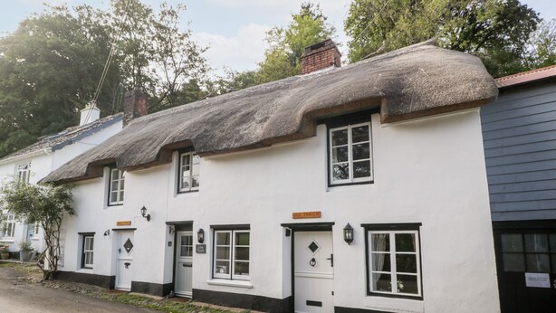 A traditional white building with black trim and a thatched roof, featuring multiple windows and doors, and a sign reading "Old Thatch." - The Old Thatch (Minehead)