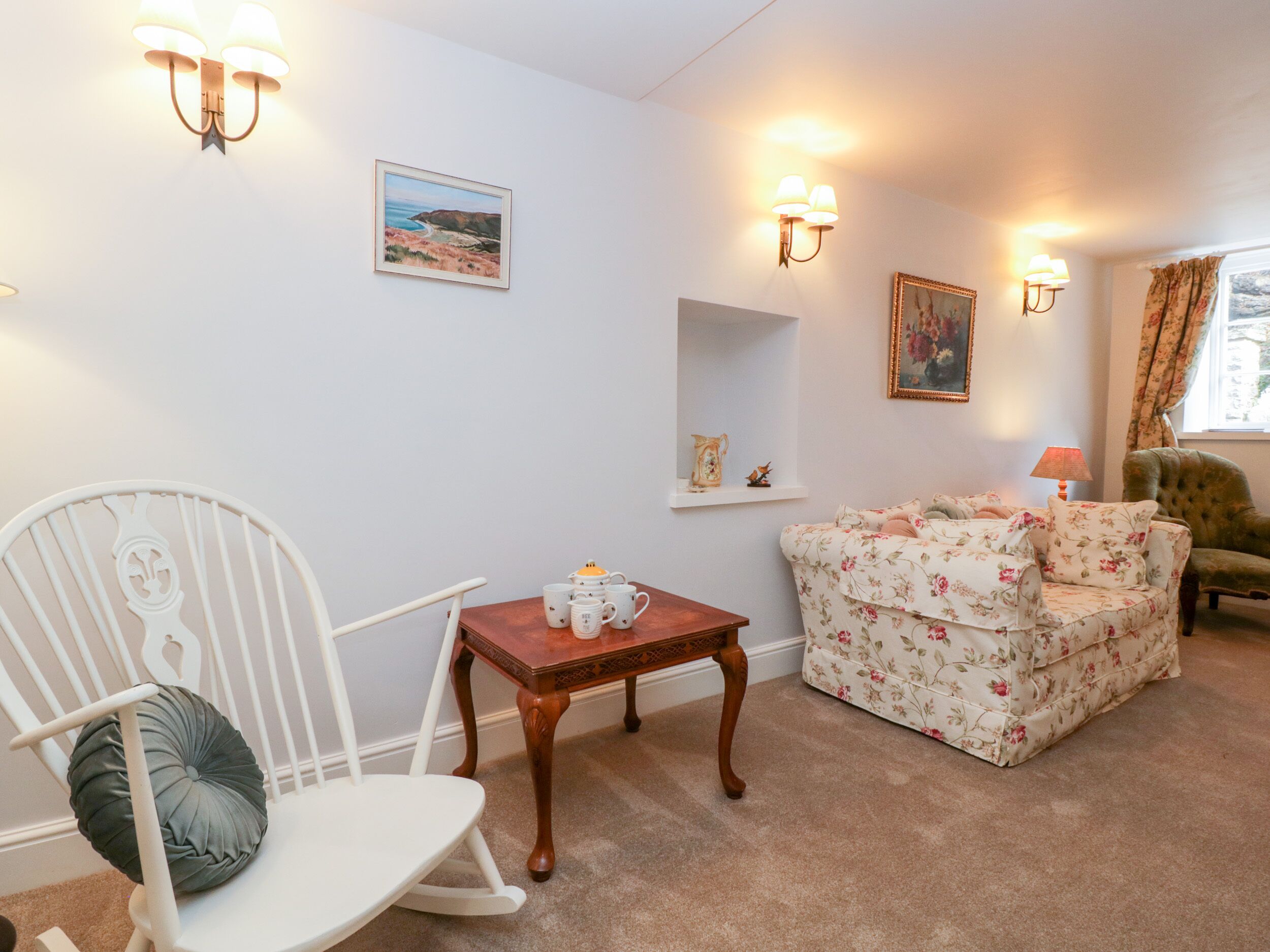 A cozy living room with a white rocking chair, a floral sofa, and a wooden coffee table.