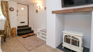 A room with a fireplace, a TV mounted on the wall, a staircase, and a door. - The Old Thatch (Minehead)