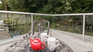 A balcony with a metal table, a red teapot, and two white mugs with bee designs. - The Old Thatch (Minehead)