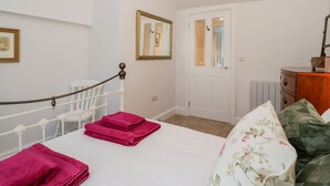 A bedroom with a bed, a white radiator, a wooden dresser, and a door with a mirror. - The Old Thatch (Minehead)