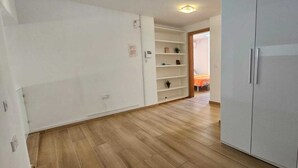 Une pièce avec un plancher en bois, une armoire blanche et une étagère où sont disposées des plantes.