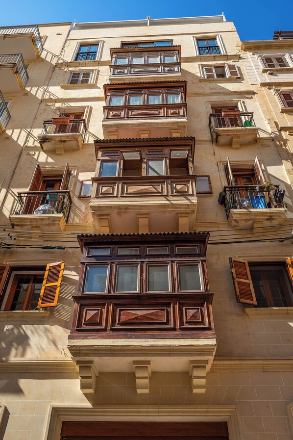 A multi-story building with balconies, windows with shutters, and a tiled facade.