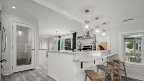 Een moderne keuken met een marmeren aanrechtblad, hanglampen en uitzicht naar buiten.