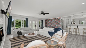 Een moderne woonkamer met een bank, salontafel en rieten stoelen. Er is een keuken met een bar en barkrukken.
