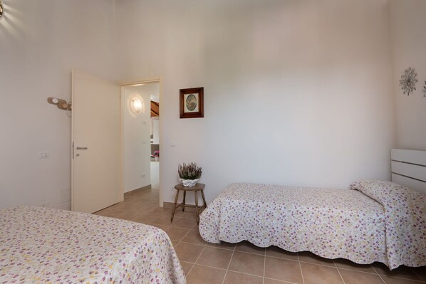 Un dormitorio con dos camas, una puerta, una mesita con una planta y un cuadro en la pared.