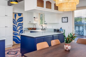 A modern kitchen with white cabinets, a blue island, and a dining area with a wooden table and chairs. - Love Garden [Spiritual Retreat] (Sedona)