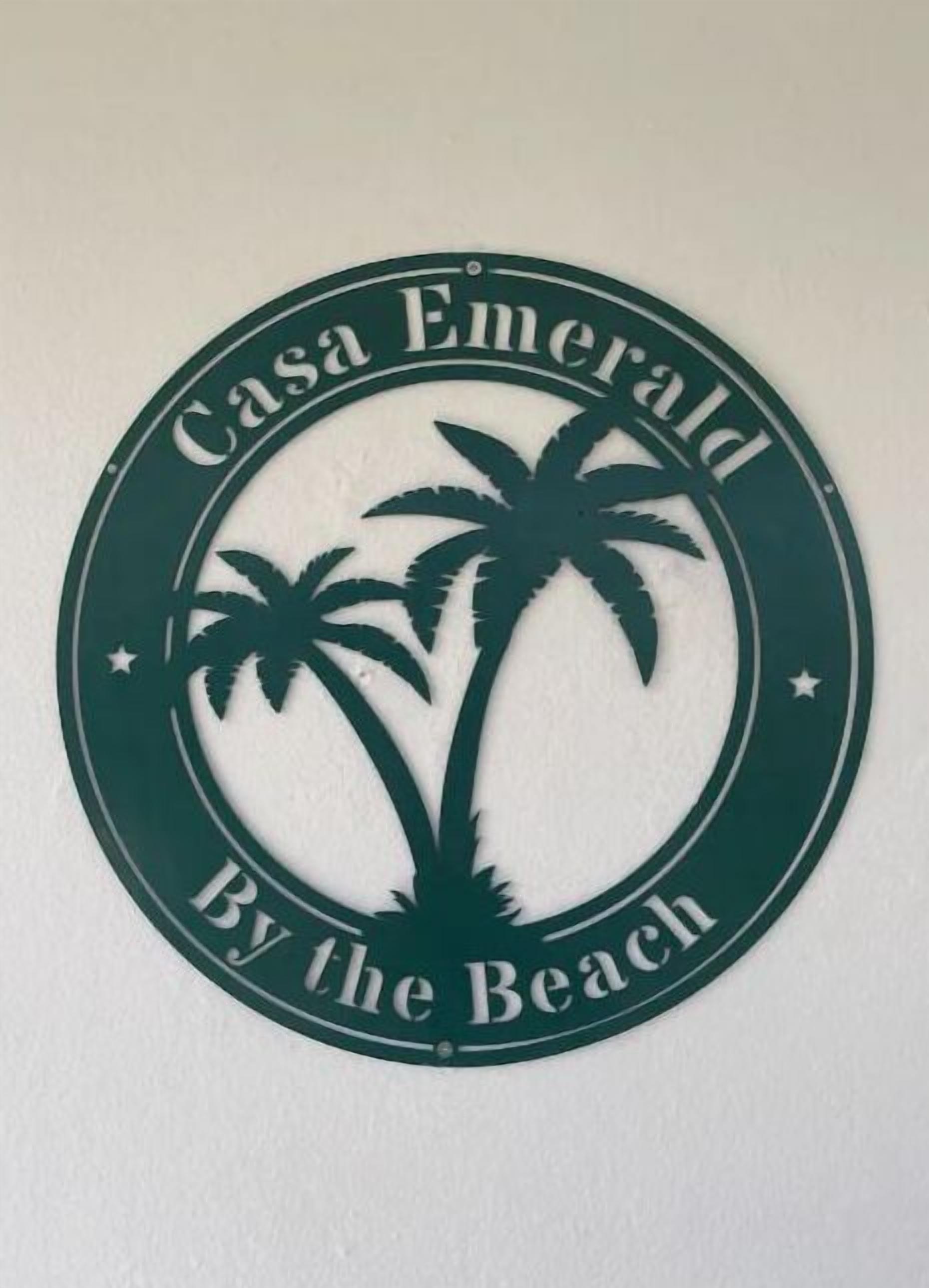 Un letrero circular con palmeras y el texto 'Casa Emerald By the Beach'.