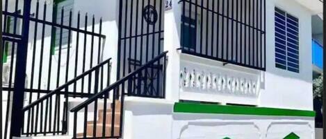 A white building with green accents, a satellite dish, and a black metal gate.