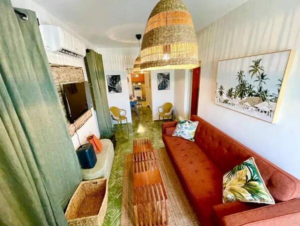 En stue med en rød sofa, en vævet lysekrone og et billede af palmer.