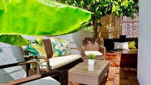 Un canapé en osier avec un coussin, une petite table avec une plante et une chaise avec un coussin.