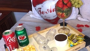 Ein Bett mit einem Tablett voller Snacks, Getränke und einem dekorativen Kissen in Herzform.