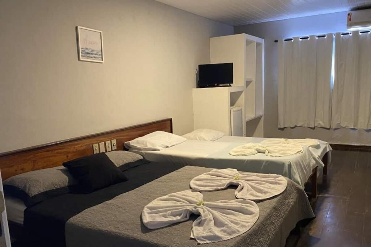 Une chambre d’hôtel avec deux lits, un téléviseur posé sur un meuble et un rideau.