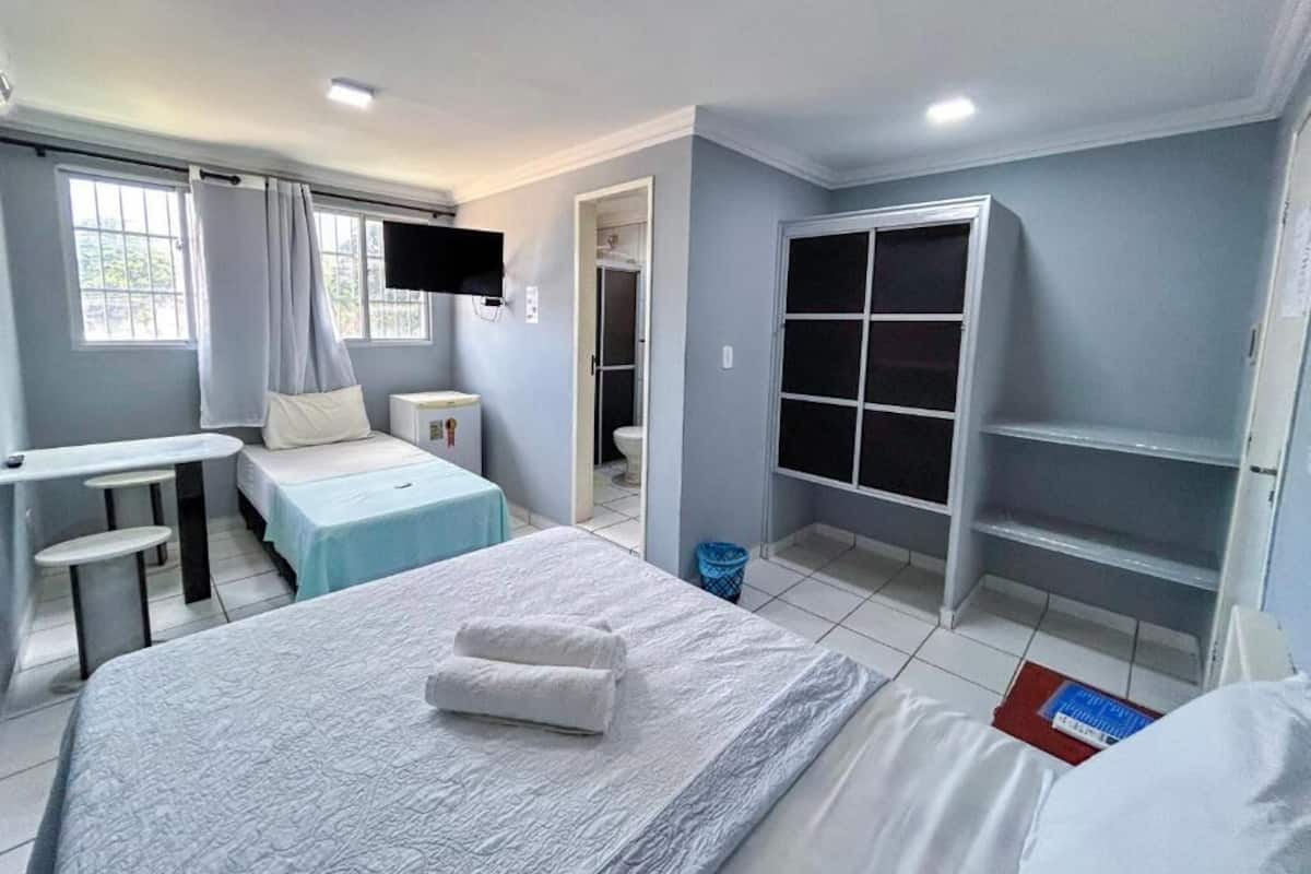 Une chambre d’hôtel avec un lit, un petit bureau, une télévision, une fenêtre et une armoire.