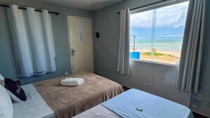 Ein Zimmer mit zwei Betten, einem Fenster mit Meerblick und einer Tür.