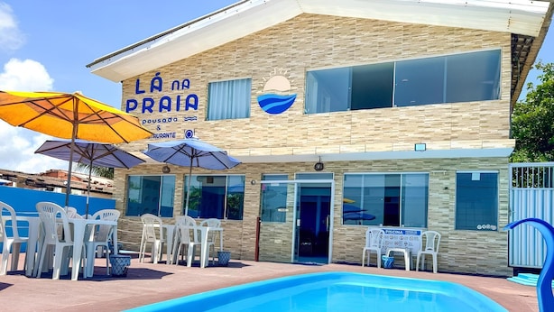 Ein Gebäude mit einem Schild, auf dem 'LA NA PRAIA pousada & restaurant' steht, und einem Poolbereich mit Stühlen und Sonnenschirmen.