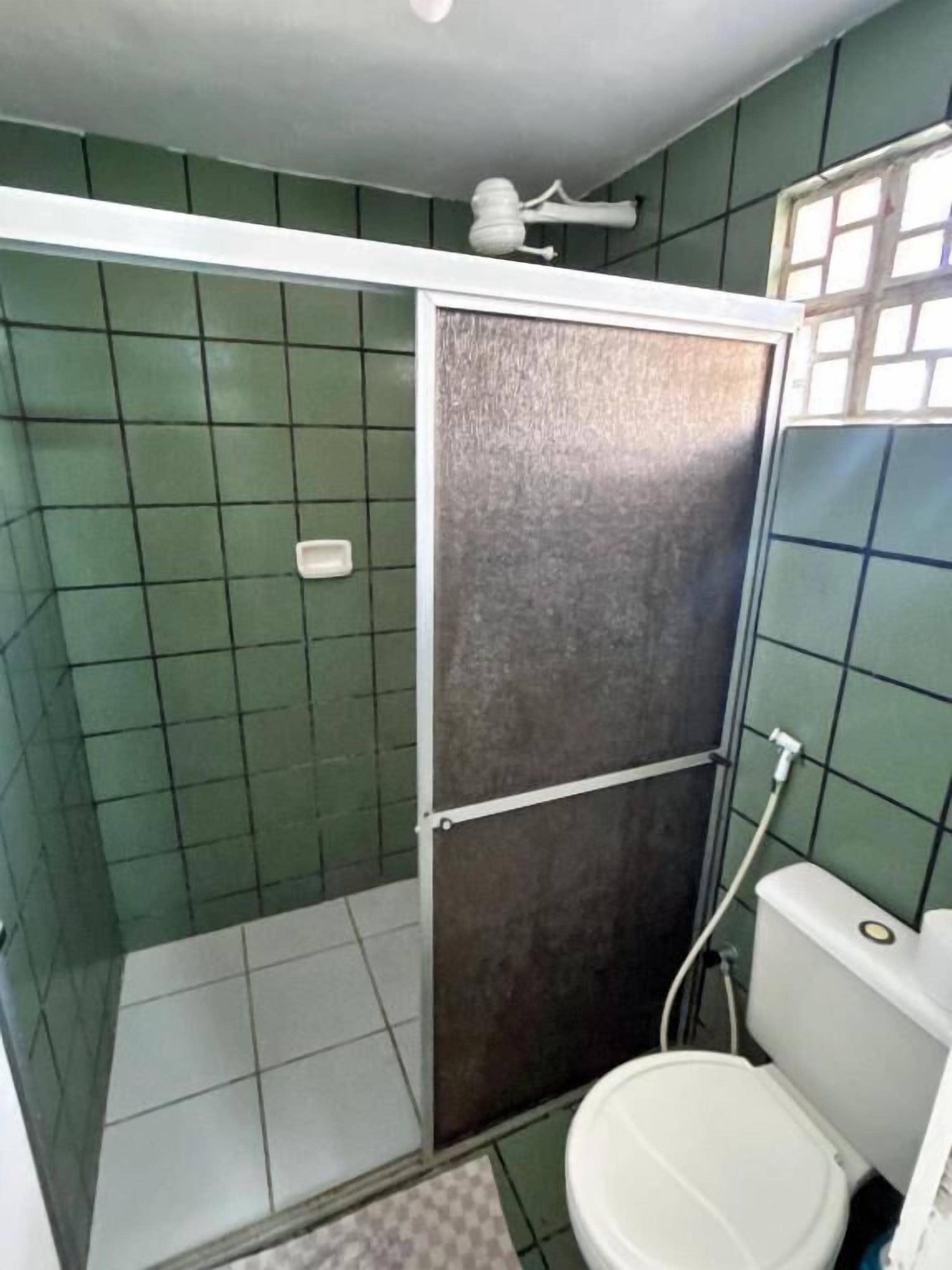 A bathroom with green tiles, a white toilet, and a shower enclosure.