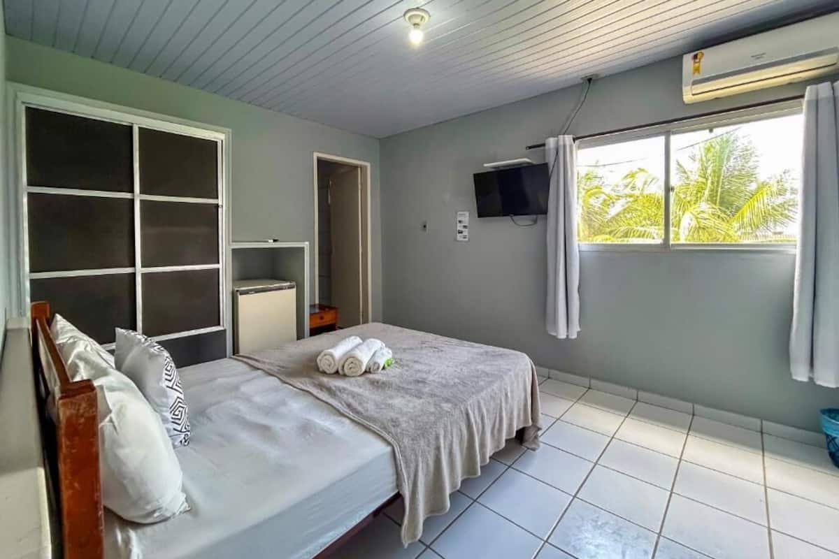 Une chambre à coucher avec un lit, une télévision, une fenêtre et un ventilateur de plafond.