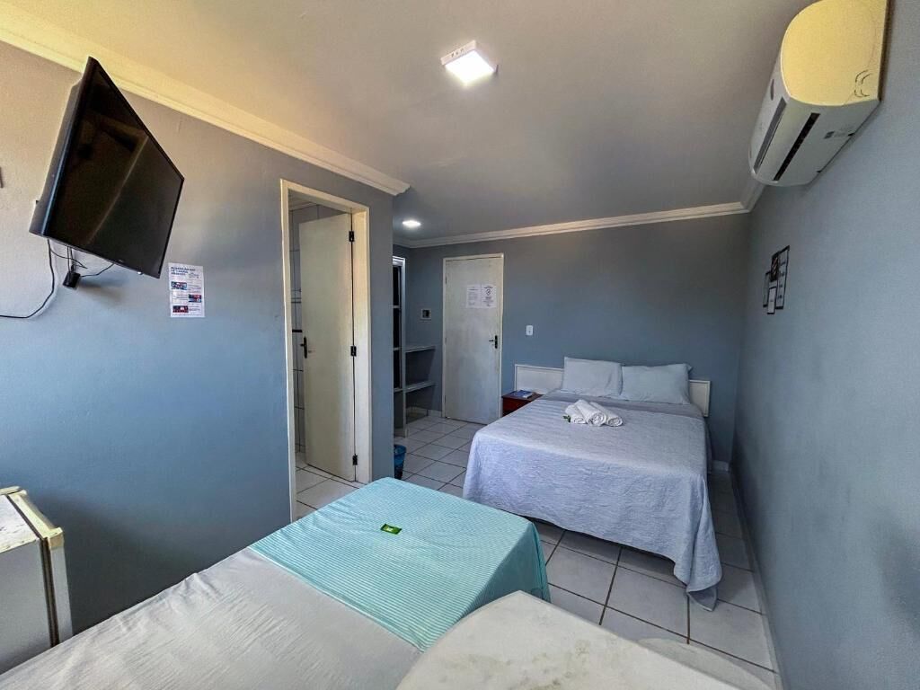 Hotellihuone, jossa on kaksi sänkyä, televisio, ilmastointilaite ja ovi, joka johtaa kylpyhuoneeseen.