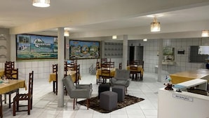 Eine Hotelhalle mit mehreren Essplätzen, Tischen und Stühlen, einem Empfangsbereich und einem großen Wandgemälde.