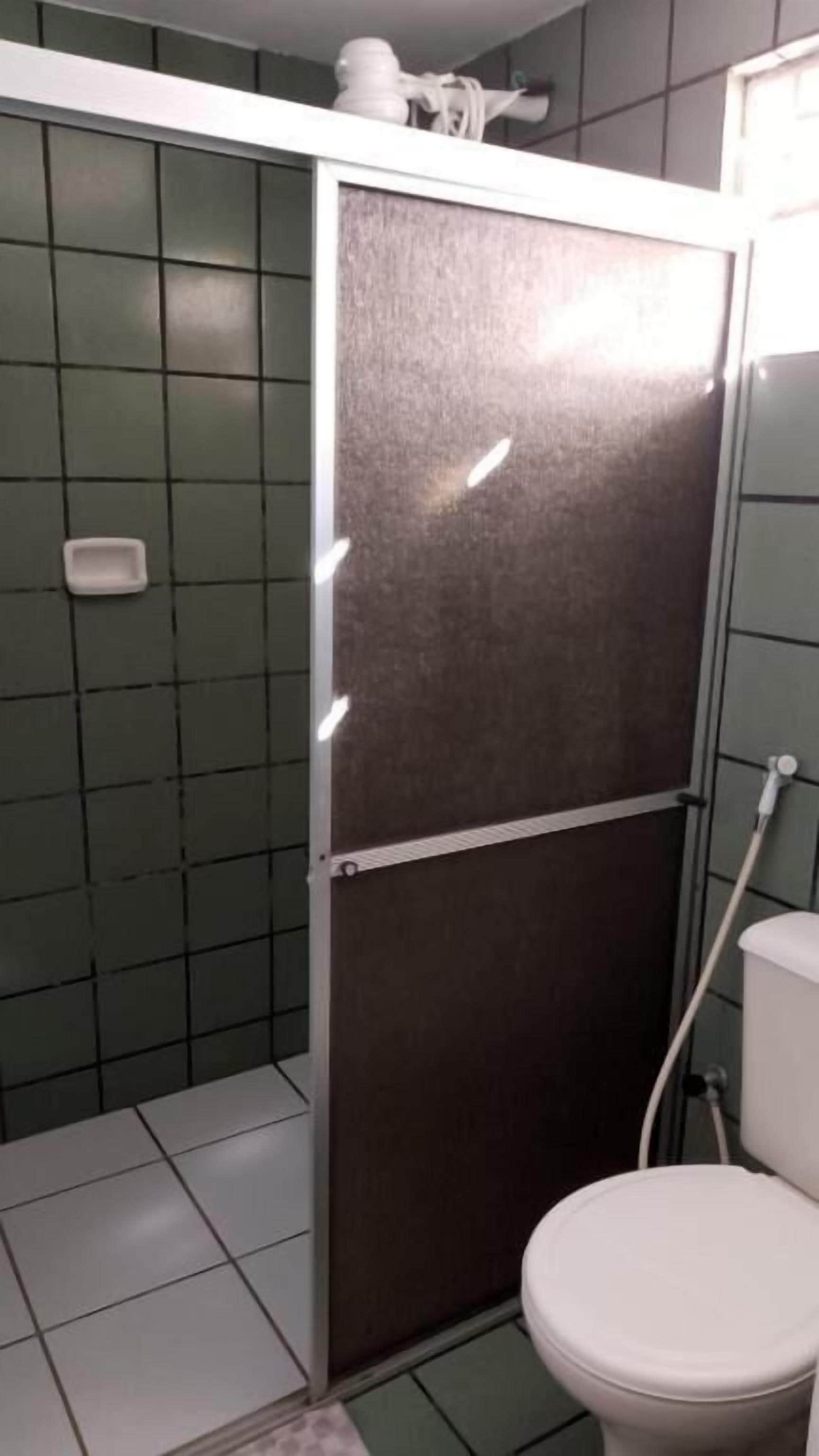 Une salle de bain comprenant des toilettes, un espace douche et un mur recouvert de carreaux.