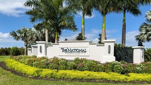 A sign for The National Golf & Country Club with a well-manicured lawn and palm trees. - Ave Maria - Relax & Golf. Golf resort with great amenities and gorgeous views. (Ave Maria)
