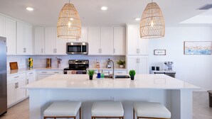 A modern kitchen with white cabinets, a large island with bar stools, a microwave, and hanging wicker pendant lights. - Ave Maria - Relax & Golf. Golf resort with great amenities and gorgeous views. (Ave Maria)