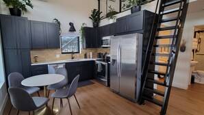 Una cocina moderna con armarios oscuros, un refrigerador de acero inoxidable, una mesa de comedor con sillas y una ventana con vistas a un área exterior nevada.