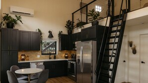 Una cocina moderna con armarios oscuros, un refrigerador de acero inoxidable, una mesa de comedor con sillas y una escalera.