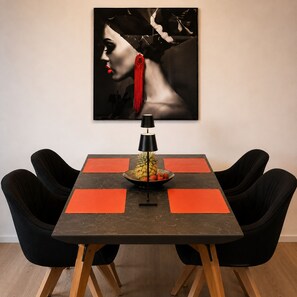 Une table à manger avec quatre chaises noires, une lampe de table noire et un saladier de fruits posé sur la table.